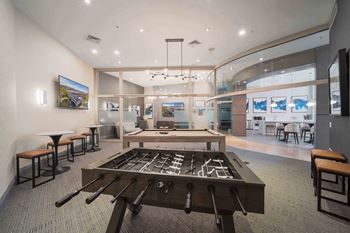 A room with a foosball table in the center and a bar area to the left.